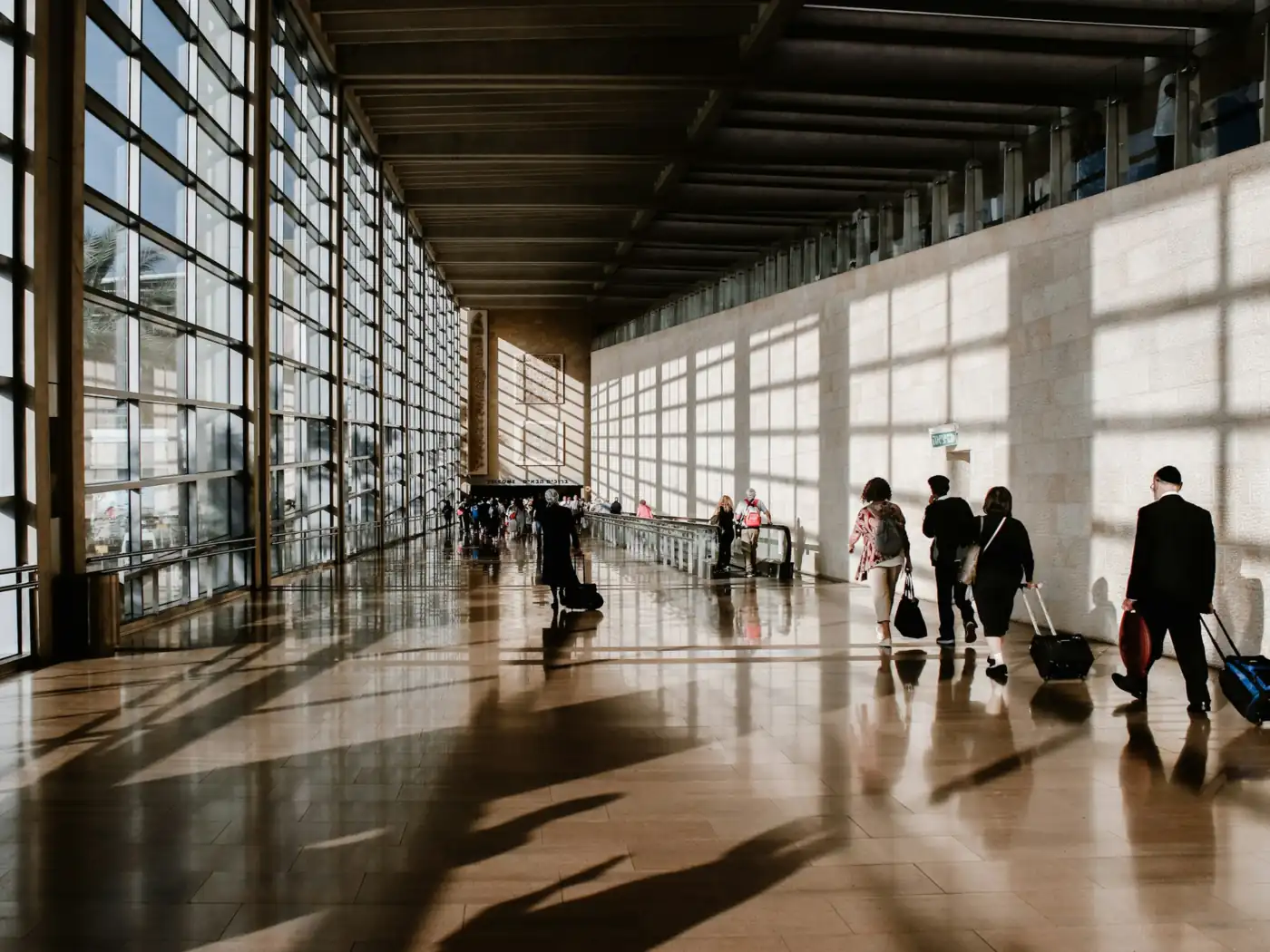 Viajeros con sus valijas caminan por la terminal luminosa de un aeropuerto.